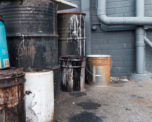 Old barrels dripping with paint and chemicals at the back of a warehouse.