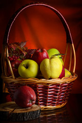 Wicker basket with autumn fruits of apples, quince and viburnum on a dark background. Beautiful autumn still life