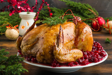 Whole roasted chicken with cranberry sauce on white plate on wooden table with Christmas decoration