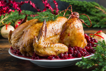 Whole roasted chicken with cranberry sauce on white plate on wooden table with Christmas decoration