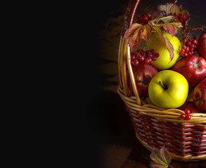 Wicker basket with autumn fruits of apples, quince and viburnum on a dark background. Beautiful autumn still life. Place for your text