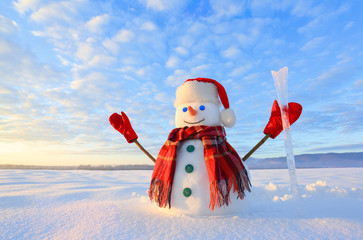Unbelievable sunrise. Happy snowman in hat, scarf, red gloves with ice pikestaff is standing on the...