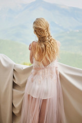 Fototapeta na wymiar silhouette of young beautiful girl bride in a peignoir stands of the balcony overlooking the mountains