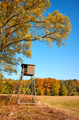 Wooden elevated deer hunting blind at the edge of a forest and field.
