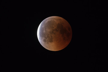Super Bloody Moon, full eclipse end phase against black sky background, Earth's shadow starting to move out from the Moon surface