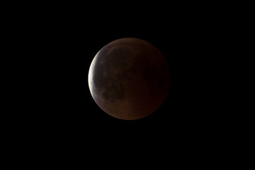 Super Bloody Moon, full eclipse end phase against black sky background, Earth's shadow starting to move out from the Moon surface