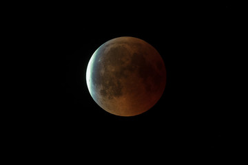 Super Bloody Moon, full eclipse end phase against black sky background, Earth's shadow starting to move out from the Moon surface