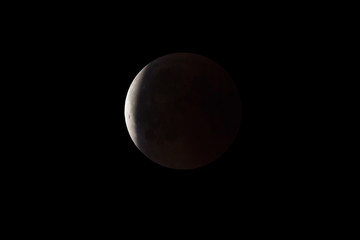 Super Bloody Moon, full eclipse end phase against black sky background, Earth's shadow starting to move out from the Moon surface