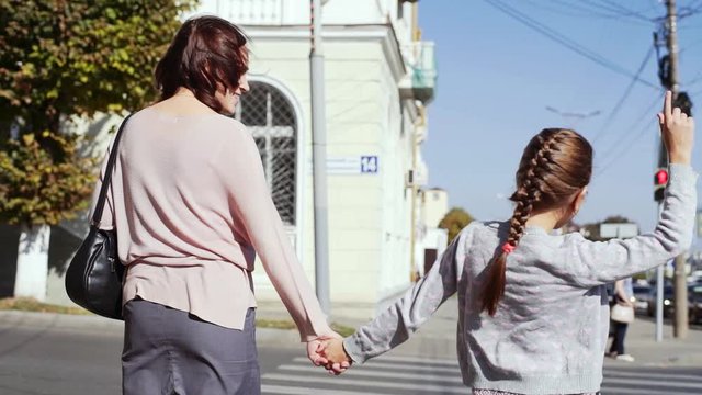 A young woman with a 10-year-old daughter crosses the road at a pedestrian crossing.