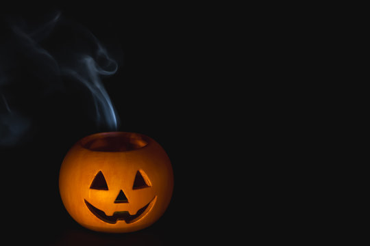 Halloween orange pumpkin with smoke coming out in front of a black background