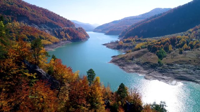 Aerial View. Autumn color forest. Colorful autumn trees, turquoise lake on a sunny fall day. Beautiful Lake in the mountains surrounded by colorful autumn forest. Crystal clear water of the lake. 