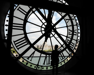 A person's silhouette behind the back of a large clock with a view of the outside 