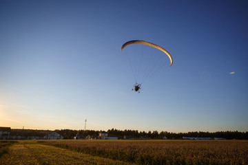 Paratrayke flight, paraglider in the sky at sunset. The wing of a parachute with a paraglider cabin flies across the sky in the setting sun