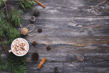 Cup of hot cocoa with marshmallows on wooden background with pine branches, pine cones, cinnamon...