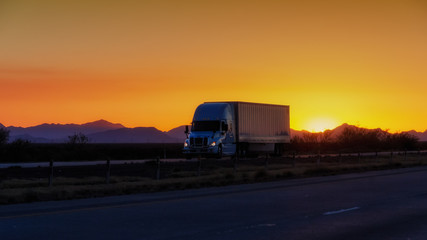 Semi-truck driving on highway at sunset with mountains in background