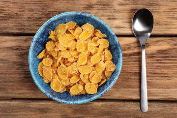 Bowl with healthy cornflakes and spoon on wooden table, top view