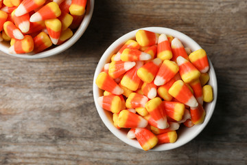 Bowl with tasty candy corns on wooden table, top view