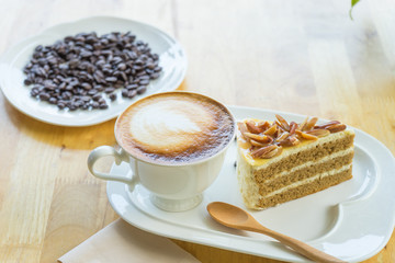 Hot coffee late in white cup on blurred raw coffee seed background, Bakery almond in plate,