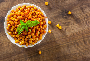 Fried spicy chickpeas in white bowl on wooden table background
