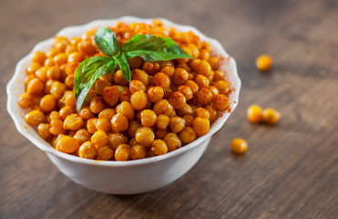 Fried spicy chickpeas in white bowl on wooden table background