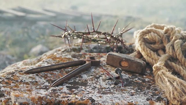 Close up of a representation of the Jesus Christ crown of thorns with nails, hammer, pliers and a rope placed on a stone.