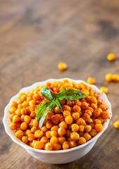 Fried spicy chickpeas in white bowl on wooden table background