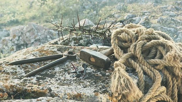 Close up of a representation of the Jesus Christ crown of thorns with nails, hammer, pliers and a rope placed on a stone.