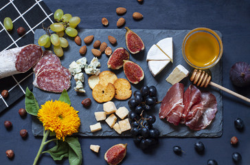 Antipasti food dark blue flat lay with nuts, honey, cured meat, salami, cheeses, grapes and figs. Top view snack concept composition