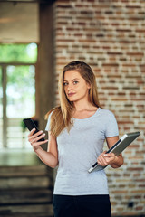 Businesswoman using smart phone while standing in cafe. In other hand holding laptop.