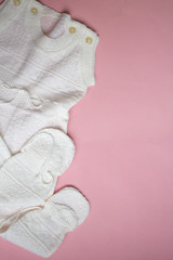 White baby's knitted clothes on pink background.