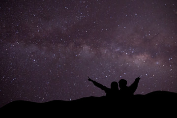 silhouette of man and woman on the mountain with blurred of milky way background.