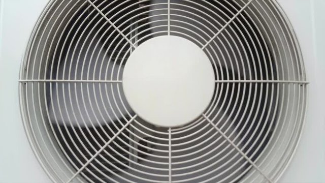 Front view of an air conditioning condenser unit with its fan spinning around