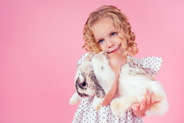 little blonde girl with a bunny rabbit easter in studio pink background.beautiful female kid celebrating Easter Holiday with pets,child painted eggs.dream and birthday present.Alice in Wonderland