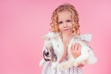 Cute little blonde girl with a bunny rabbit easter in studio pink background.beautiful female kid celebrating Easter Holiday with pets,child painted eggs in wicker basket.dream and birthday present