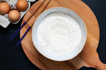 Food preparation for homemade dough for pasta or Chinese egg noodles by organic eggs and all purpose flour in a ceramic bowl with copy space.