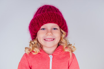charming blonde little girl big blue eyes wearing knitted red hat and cute scarf on white background in studio. Fashion autumn winter season sale concept.making a wish christmas night and birthday