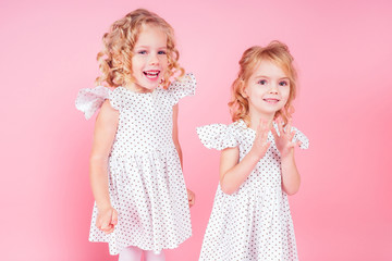 adorable baby amazed and happy smiling birthday party.two little blonde girls twin sisters in a cute white dress in the studio on a pink background,new year Christmas gift.Alice in Wonderland