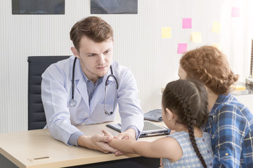 Pediatrician (doctor) man examining,reassuring and discussing child at surgery .Mother Caucasian and kid smiling in hospital room.Copy space.
