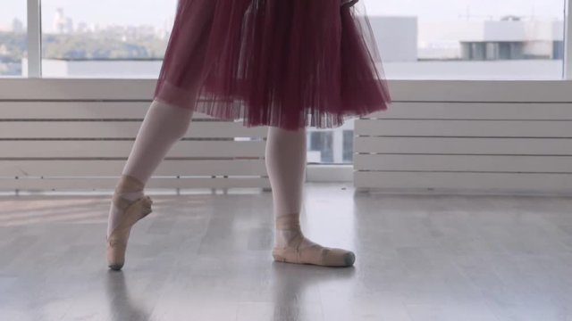 Professional ballet dancer makes battement tendu against high window background. feet in pointe close up. woman in a long red tutu on pointe. slow motion