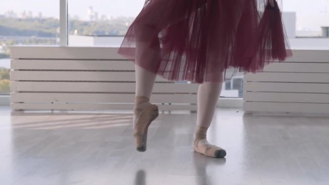 Professional ballet dancer makes battement tendu against high window background. feet in pointe close up. woman in a long red tutu on pointe. slow motion