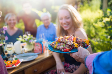 cheerful family gathered around a table for a bbq in the garden - obrazy, fototapety, plakaty