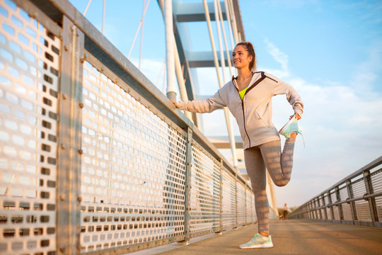 Fit woman in running clothes streching on a bridge