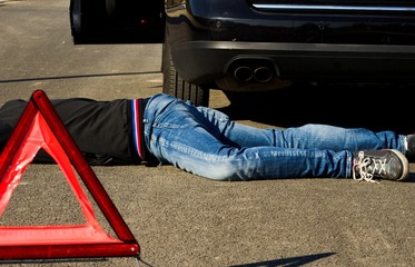 The man lies on the road behind the black car and warning triangle.The car collided pedestrian was...