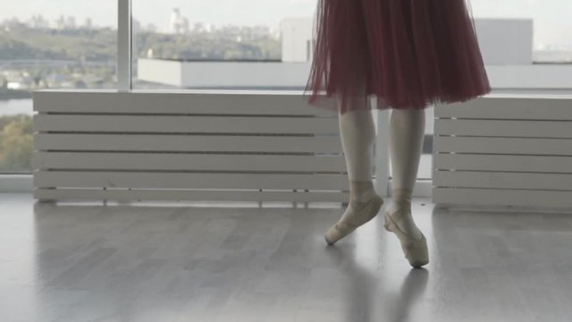 Professional ballet dancer makes battement tendu against high window background. feet in pointe close up. woman in a long red tutu on pointe. slow motion