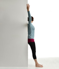 Woman exercising doing postnatal workout. Female fitness instructor stretching her spine near wall...