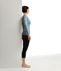 Woman exercising doing postnatal workout. Female fitness instructor stretching her spine near wall...