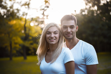 Cute loving couple standing on grass in nature green park with beautiful sundown light. Looking camera.