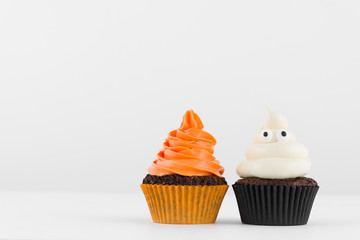 Festive close-up view of decorative homemade Halloween white and orange frosted cupcakes with eyes on white background. Text space concept.