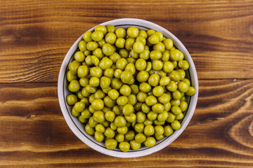 Bowl with canned green peas  on wooden table. Top view