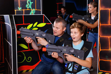 Fototapeta na wymiar Happy teen boy with laser gun having fun on lasertag arena with his father